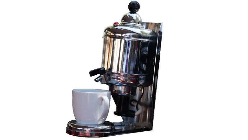 Chrome coffee maker with a white cup positioned below its spout