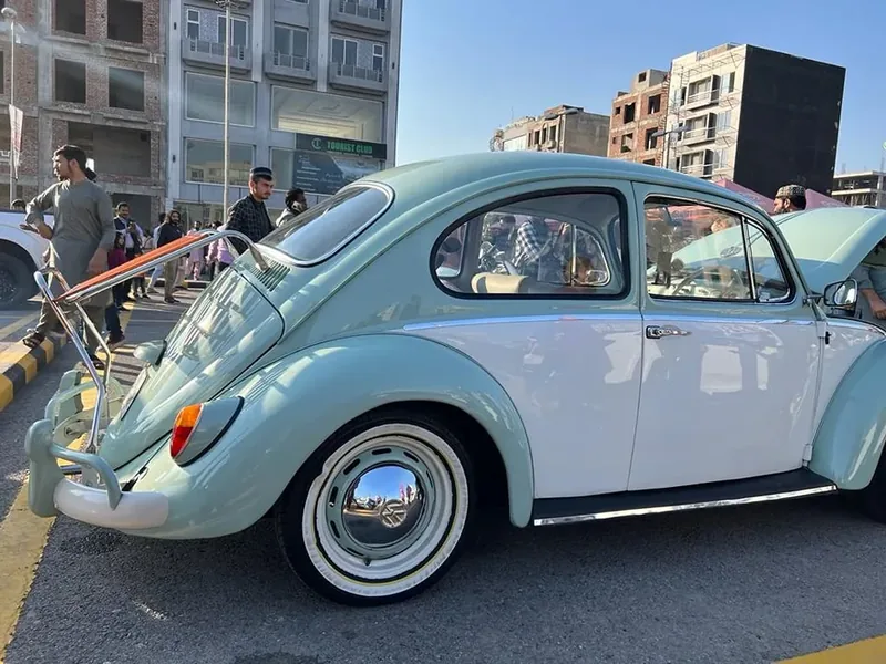 Pale green and white Volkswagen Beetle with its red-slatted deck-lid rack raised
