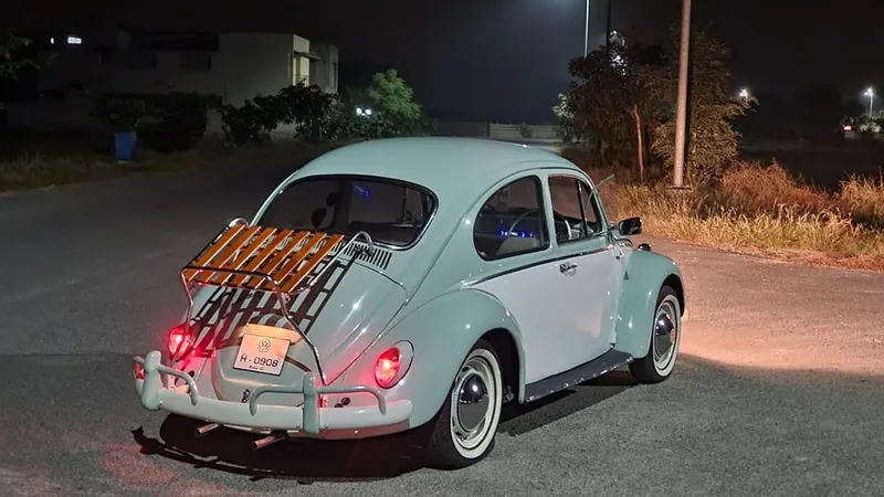 Rear three-quarter night view of a pale Volkswagen Beetle with a red-slatted deck-lid rack