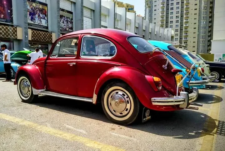 Rear three-quarter view of a red Volkswagen Beetle with a blue-slatted deck-lid rack