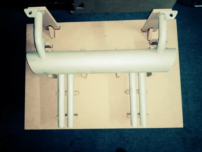 White-painted exhaust assembly with four outlet pipes on a cardboard support