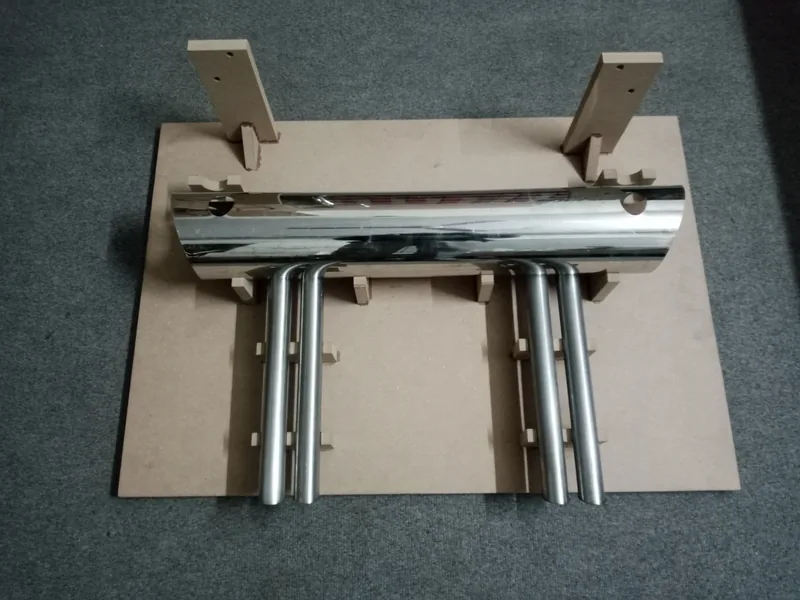 Close overhead view of a chrome four-tip exhaust assembly on a cardboard jig