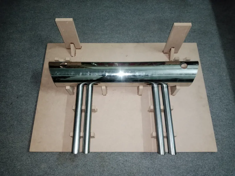 Full overhead view of a chrome four-tip exhaust assembly on a cardboard jig
