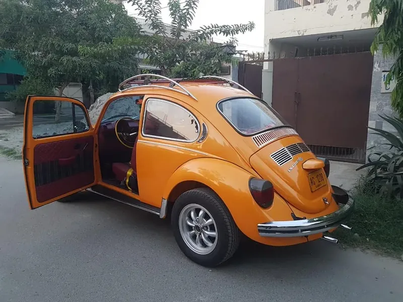 Rear three-quarter view of an orange Volkswagen Beetle with an open door and roof rack