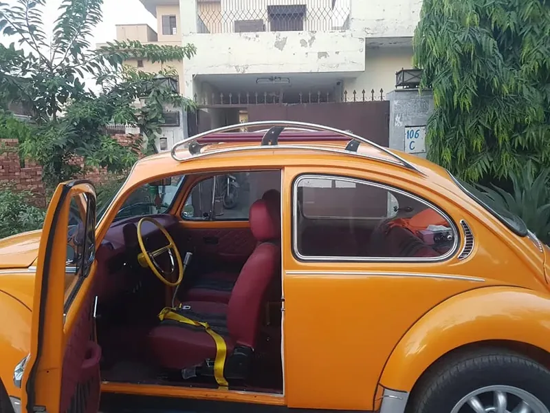 Side view of an orange Volkswagen Beetle with an open door and fitted roof rack