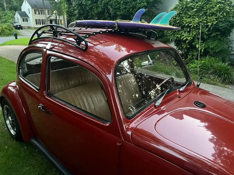 Burgundy Volkswagen Beetle with surfboards secured to a black roof rack