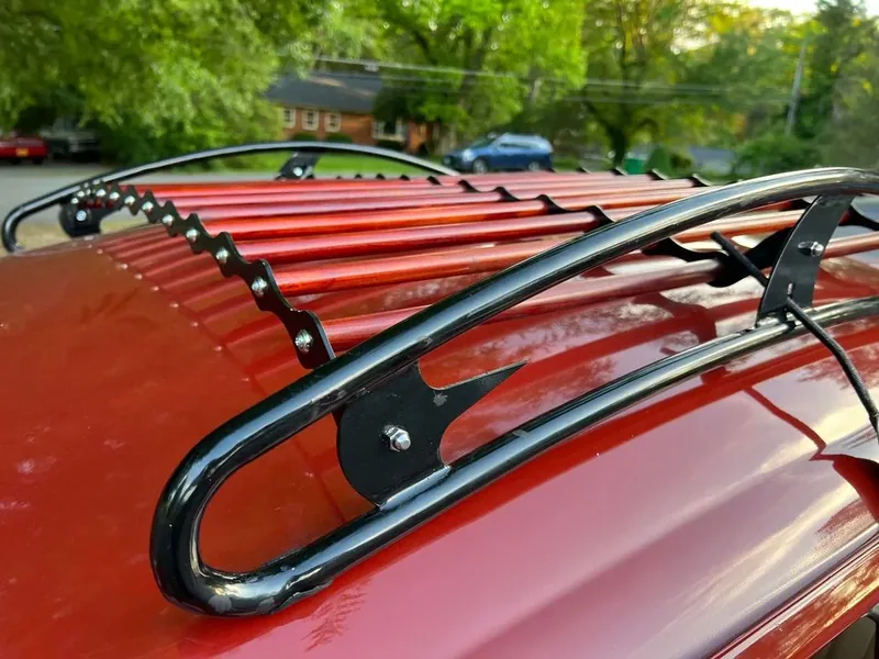 Front corner of a black roof rack with red slats fitted to a red Volkswagen Beetle