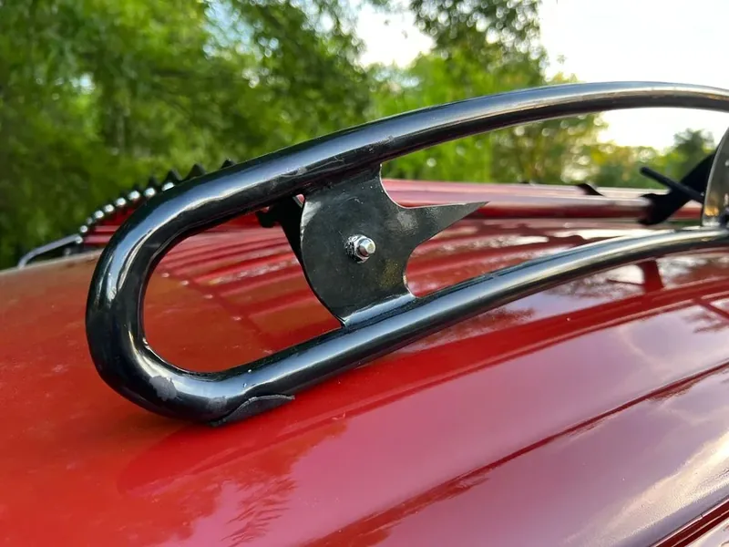 Curved black roof-rack rail and bolted bracket on a red Volkswagen Beetle