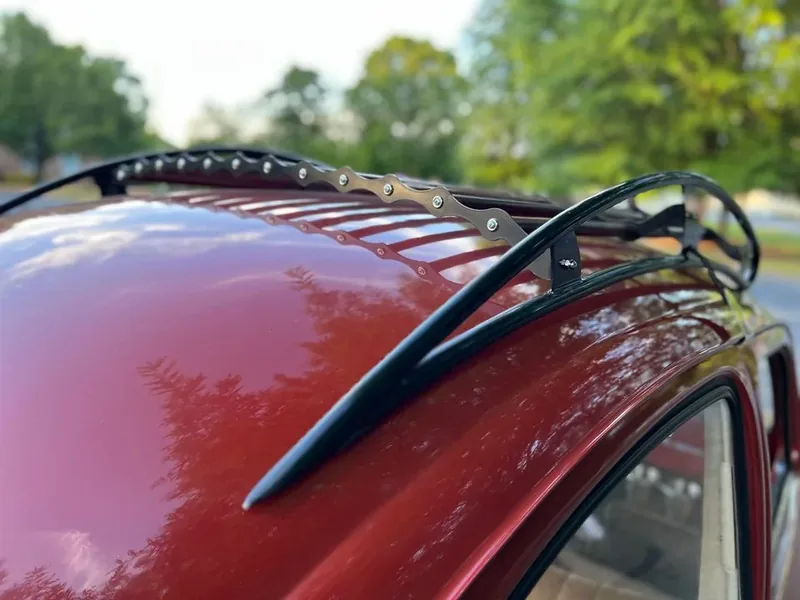 Black roof-rack side rail running along the roof of a red Volkswagen Beetle