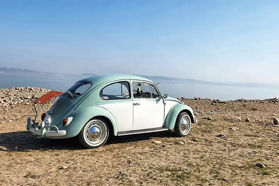 White VW Beetle with deck-lid rack near open landscape