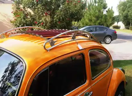 Galerie de toit chromée et rouge installée au-dessus des vitres latérales d'une orange Volkswagen Beetle